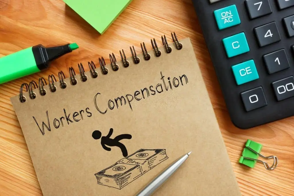 workers compensation written on a notebook cover next a calculator and highlighter